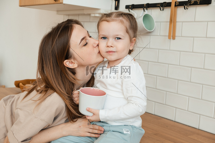 母亲在厨房里亲吻女儿，吃早餐。
