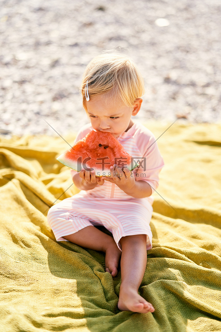 小女孩在圆石滩上的毯子上吃西瓜