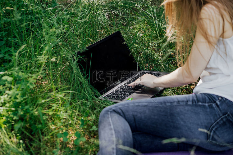 女孩坐在草地上，在笔记本电脑前