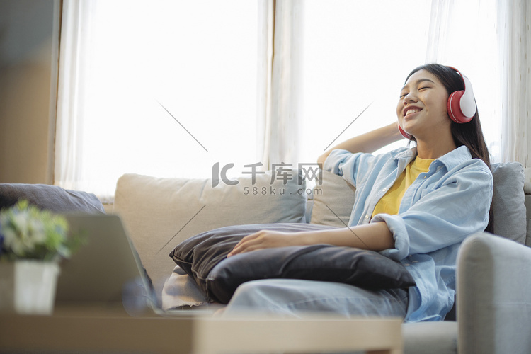 快乐的亚洲女人靠在沙发上听音乐