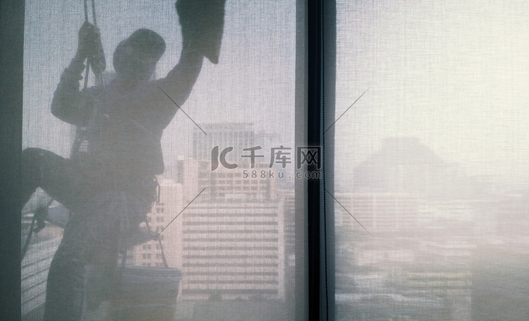 男子清洁办公楼窗户的剪影图像