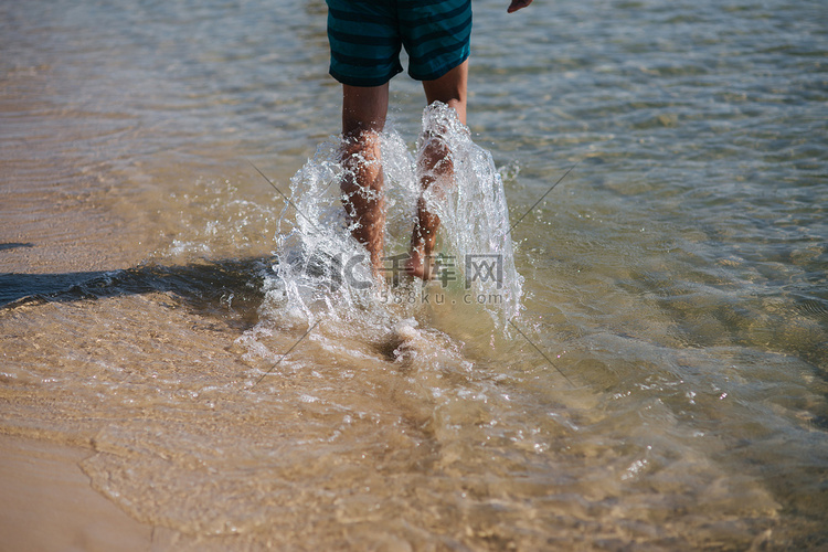 男人赤脚走在夏日海滩上的背影。