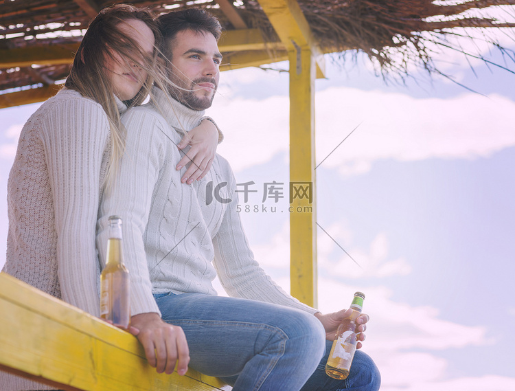 年轻夫妇在沙滩上一起喝啤酒
