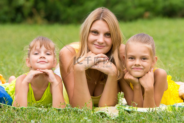 母亲和两个女儿躺在绿草上，双手