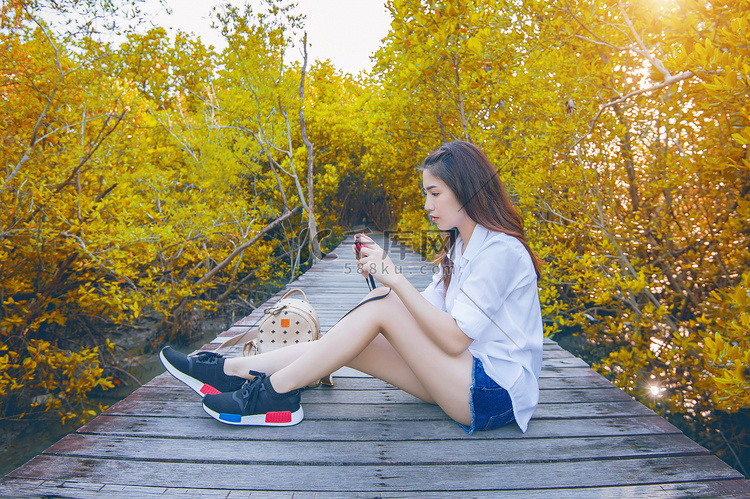 秋天，女孩独自坐在木桥上，手拿