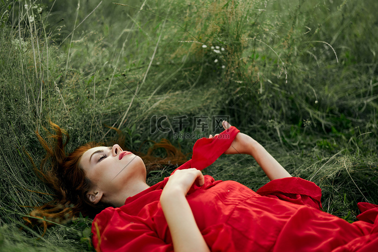 穿着红色连衣裙的漂亮女人躺在田