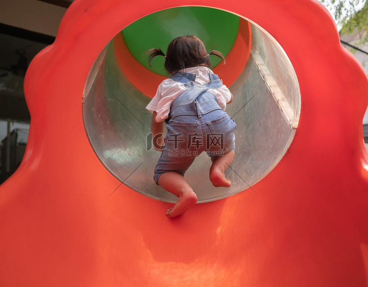 亚洲小女孩试图爬进公园操场的红