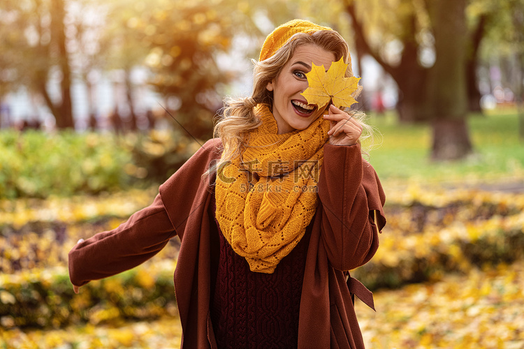 笑得开心的女人用黄色的叶子遮住