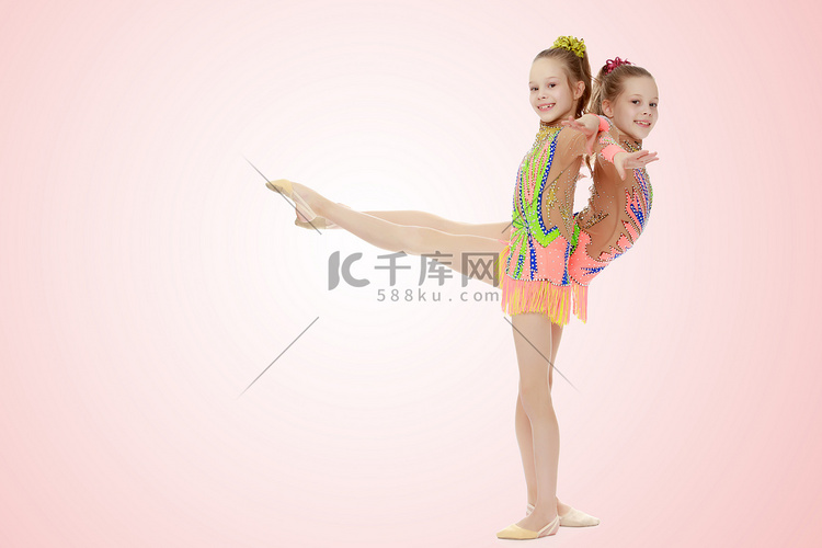 两个女孩体操运动员坐在劈叉上。