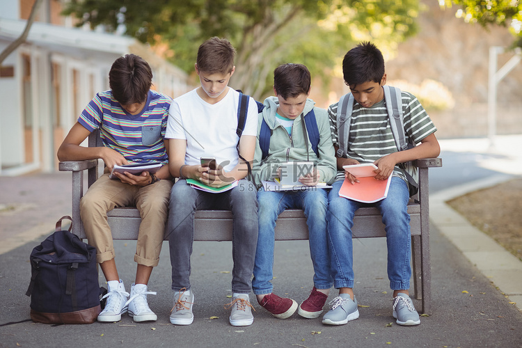 小学生在长凳上使用手机和数字平