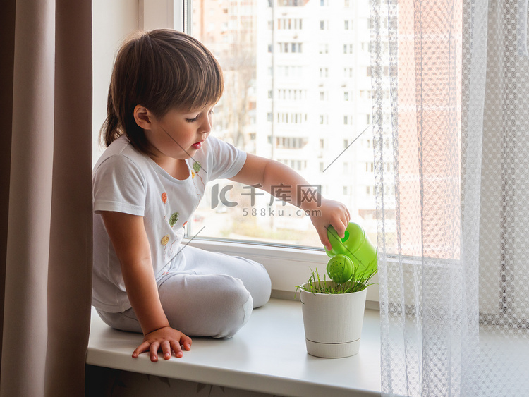 蹒跚学步的男孩坐在窗台上，浇花