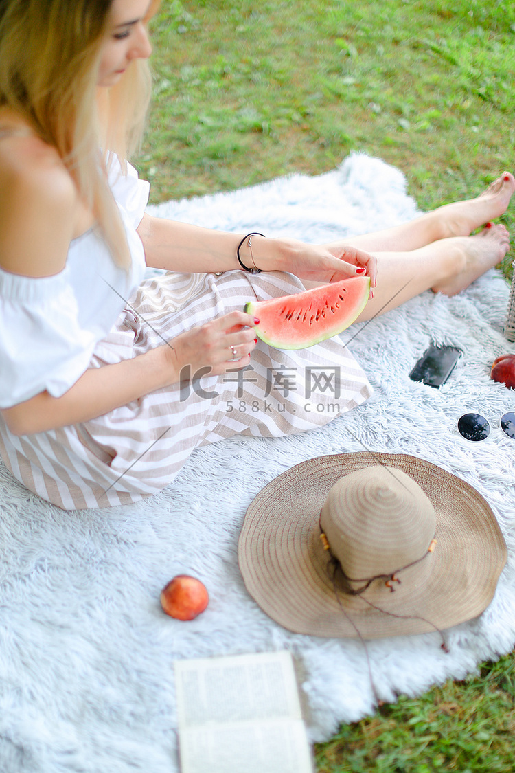 年轻的金发女孩坐在靠近水果和帽