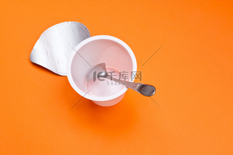 橙色背景上带勺子的空干净酸奶杯
