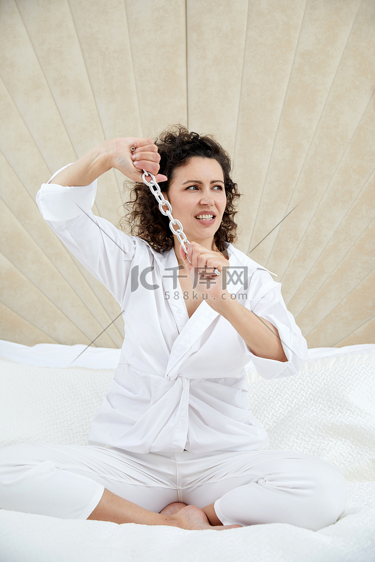 年轻漂亮的黑发卷发女人坐在白床