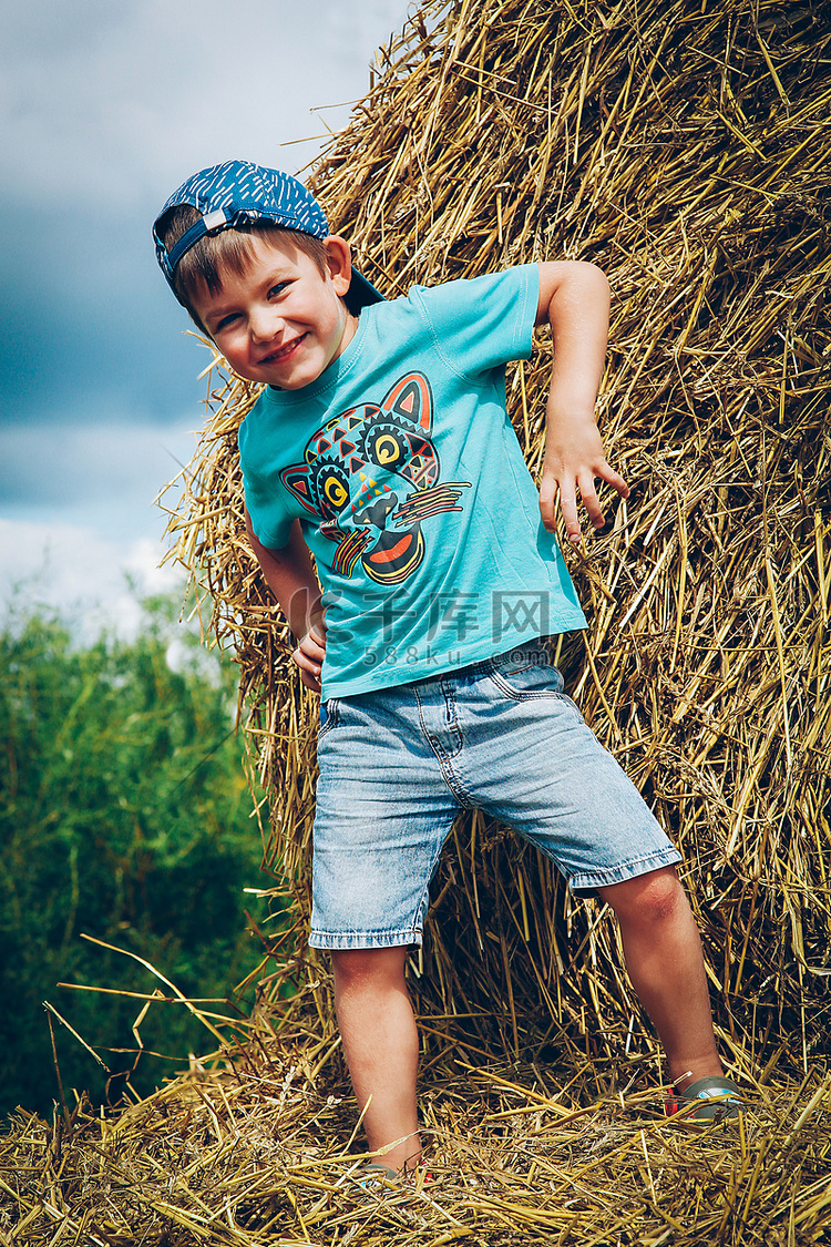 夏日戴棒球帽的男孩在稻草捆上玩