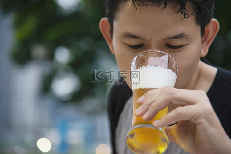 亚洲男人在绿色花园餐厅喝啤酒