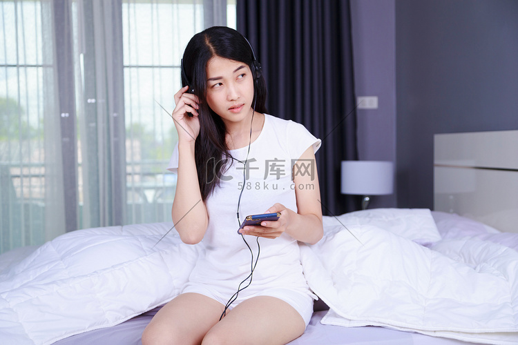戴耳机的女人在卧室的床上用智能