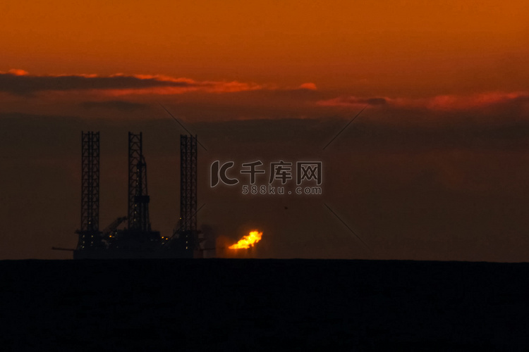 在日落时的石油平台与燃烧的火炬