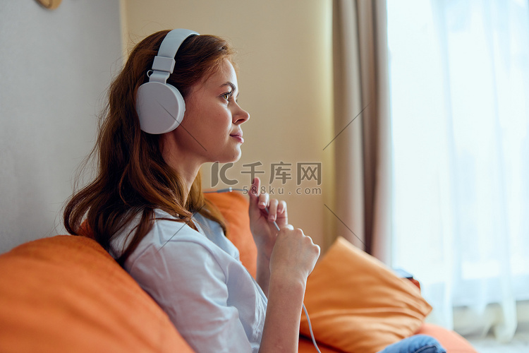 快乐的女人在橙色沙发技术上用耳