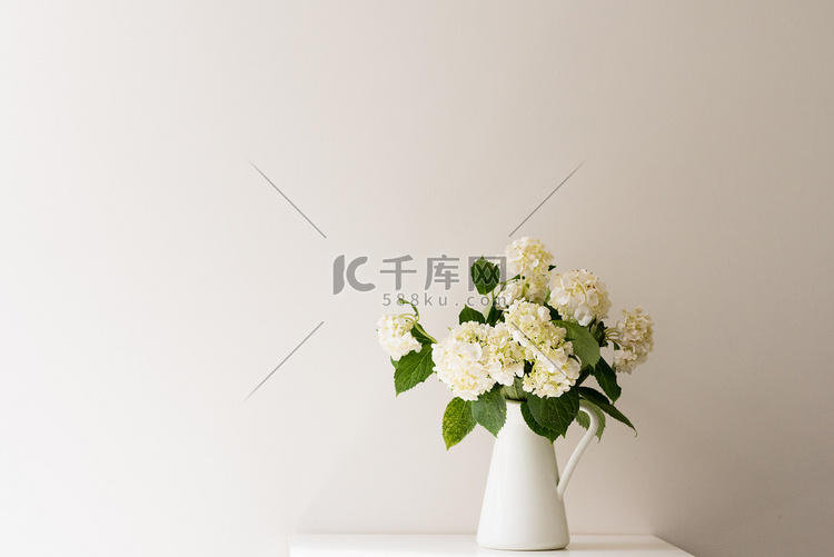 桌子上的水罐里的白色绣球花靠着