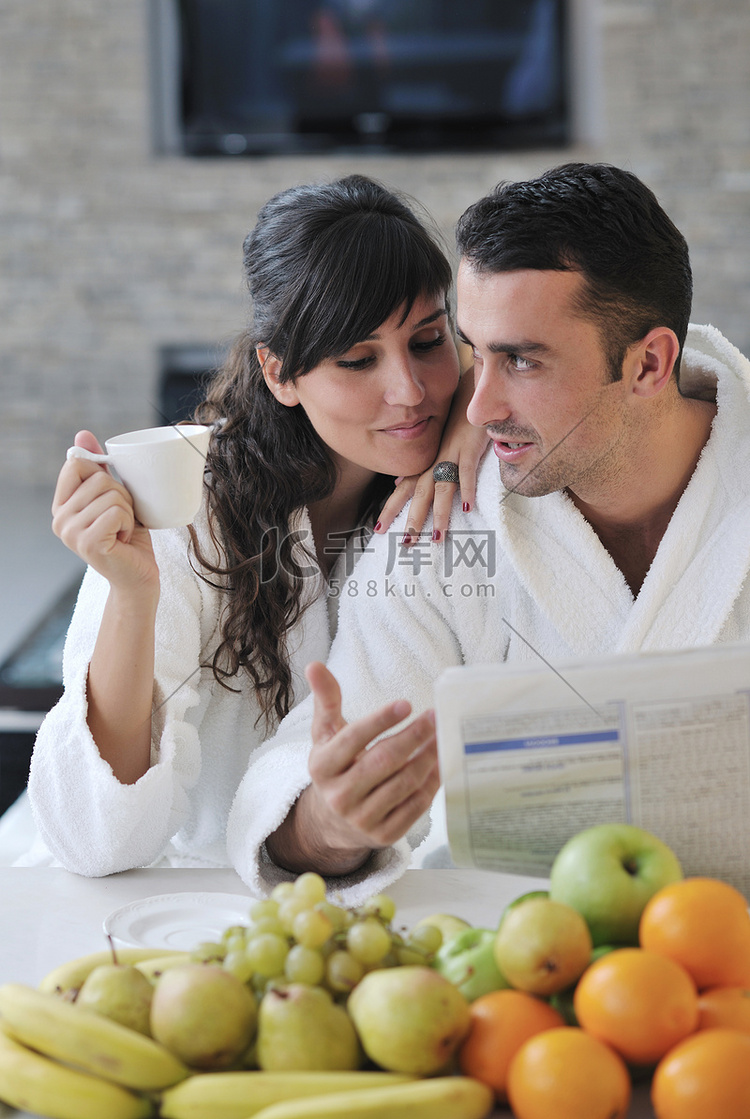 幸福的夫妇在厨房吃早餐时看报纸