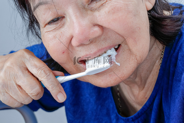 亚洲老妇尝试使用牙刷，手颤抖。