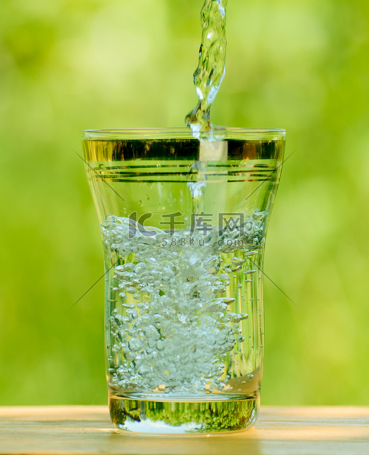 在绿色背景下将水倒入玻璃杯中
