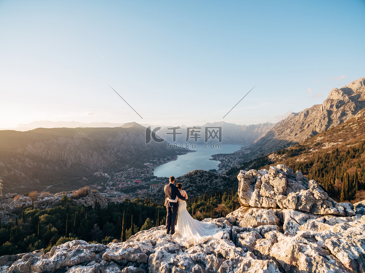 新娘和新郎站在山顶互相拥抱，眺