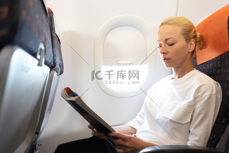 在飞机上阅读飞行杂志的女人。
