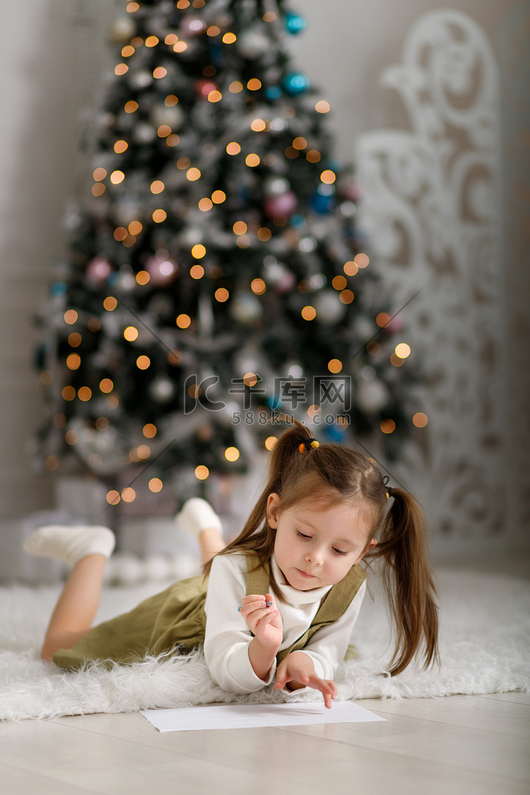 小女孩正在圣诞树的背景下给圣诞