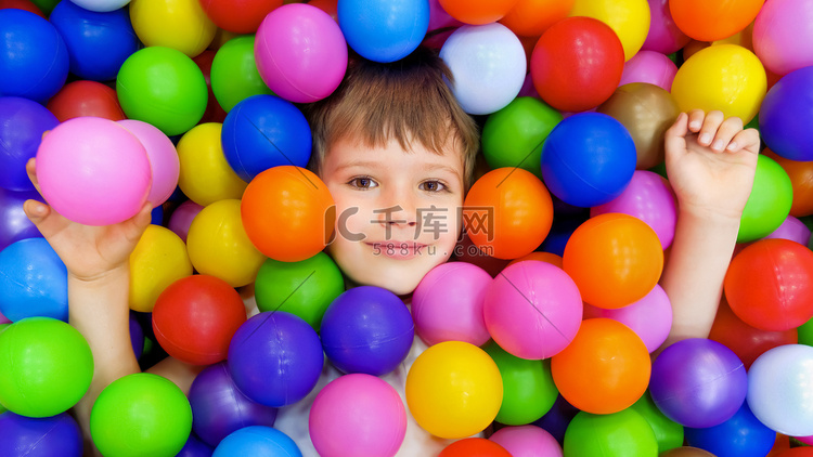 微笑的孩子躺在彩色塑料球池里。