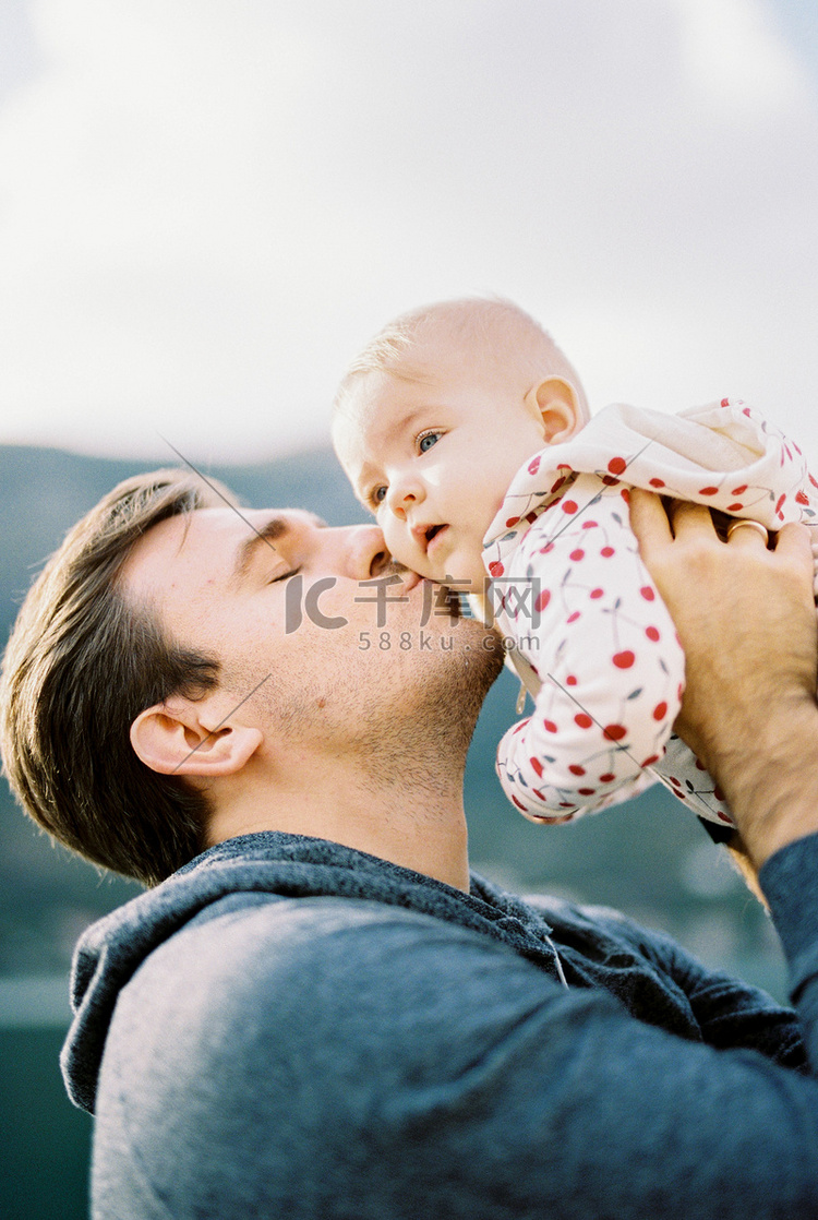 爸爸把婴儿举过头顶，亲吻他的脸