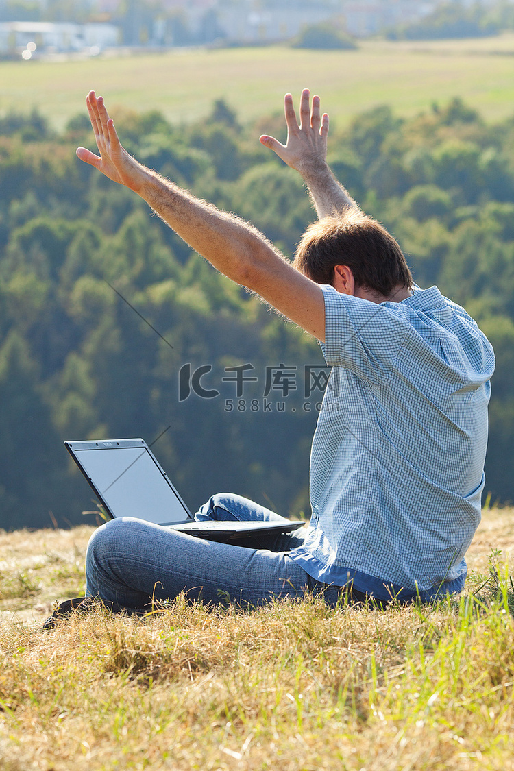 坐在山坡草地上使用笔记本电脑的