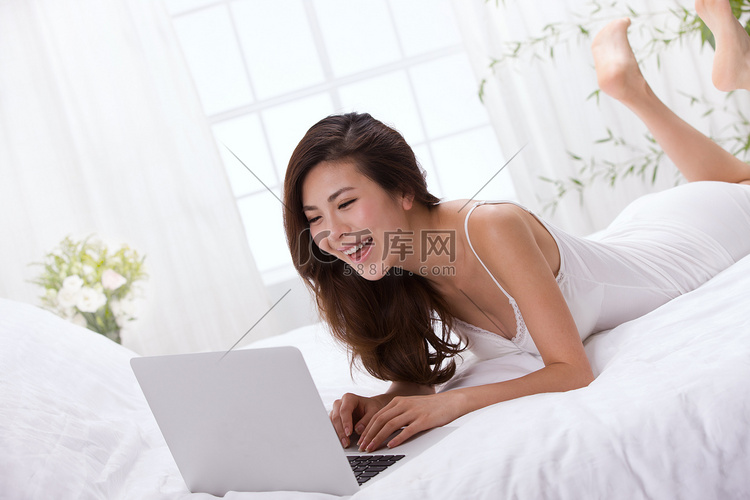 年轻女人趴在床上看笔记本电脑