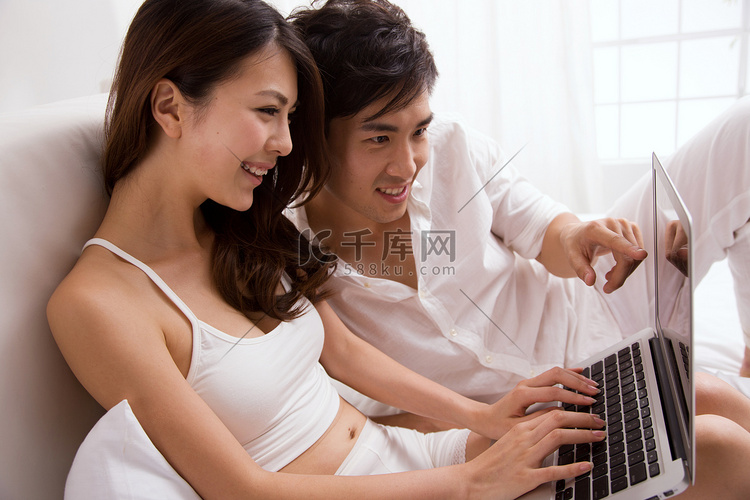 东方年轻夫妇坐在床上看电脑