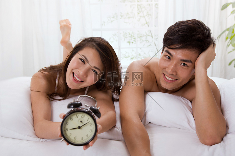 年轻夫妇趴在床上拿着闹钟