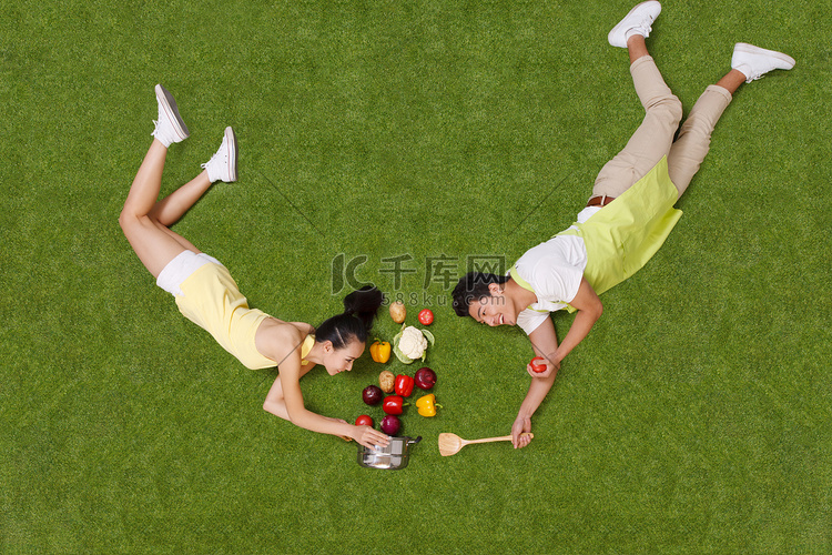 青年男女拿着蔬菜躺在草地上