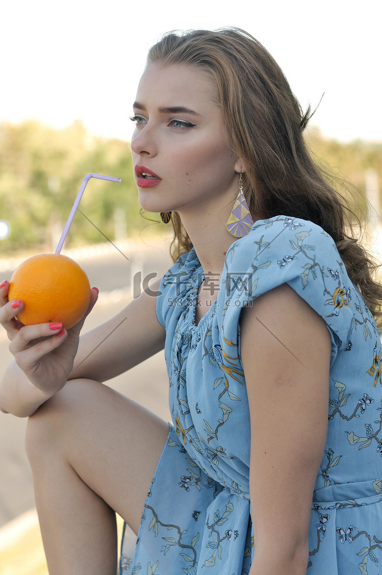 漂亮的女孩从桔子喝果汁吸管