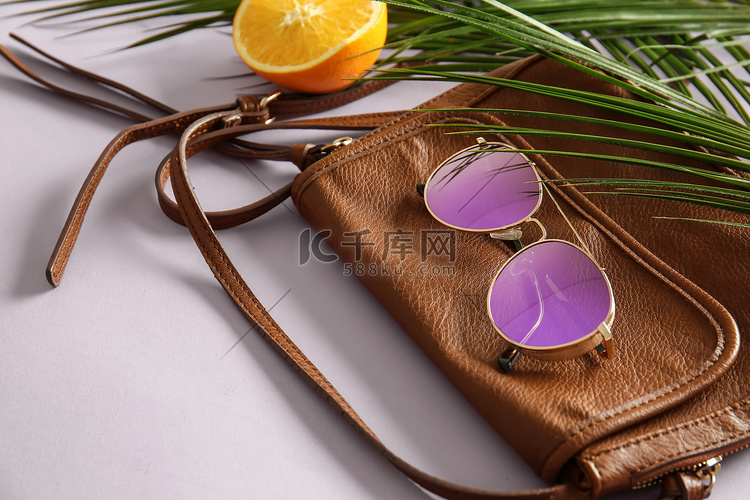 时尚的太阳镜与女性包和热带叶子