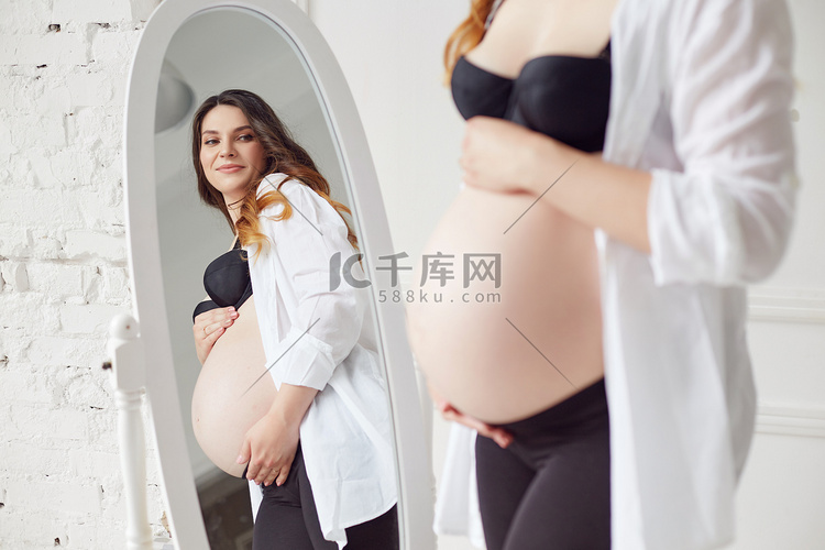 怀孕的女人看着镜子摸她的肚子。