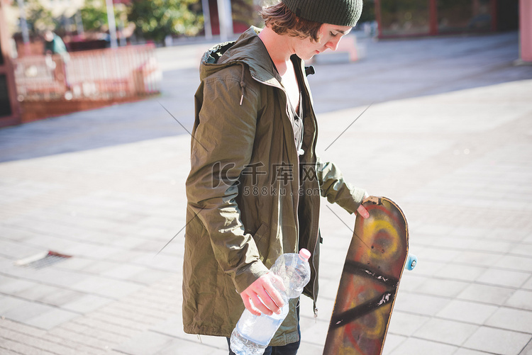 年轻的城市男性滑板手拿着一瓶水