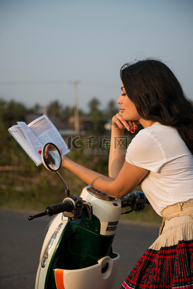 骑着轻便摩托车看书的女人