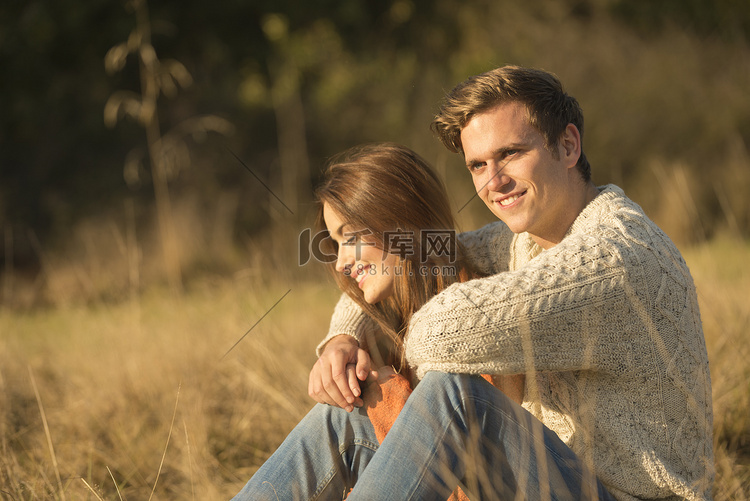 一对年轻夫妇坐在乡下面带微笑