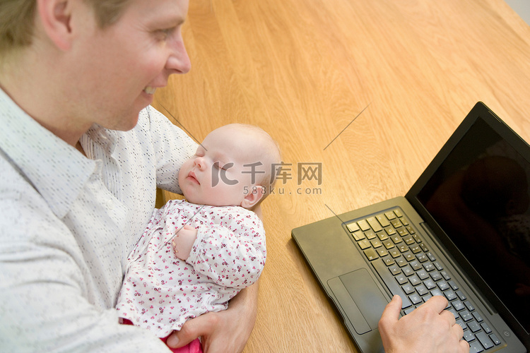 父亲带着婴儿在笔记本电脑上工作