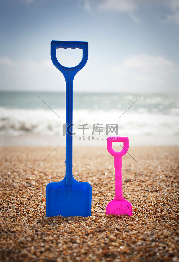 蓝色和粉色的铁锹立在海滩的沙子