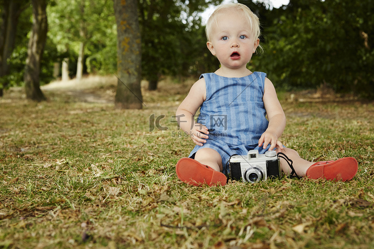坐在草地上的女婴拿着胶卷相机张