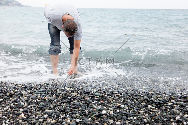 一名男子在岩石海滩上捡鹅卵石