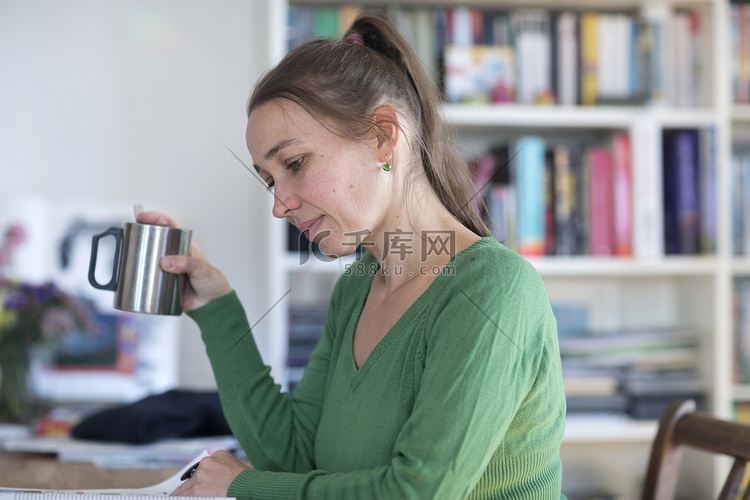 中年妇女坐在桌子旁阅读杂志托杯