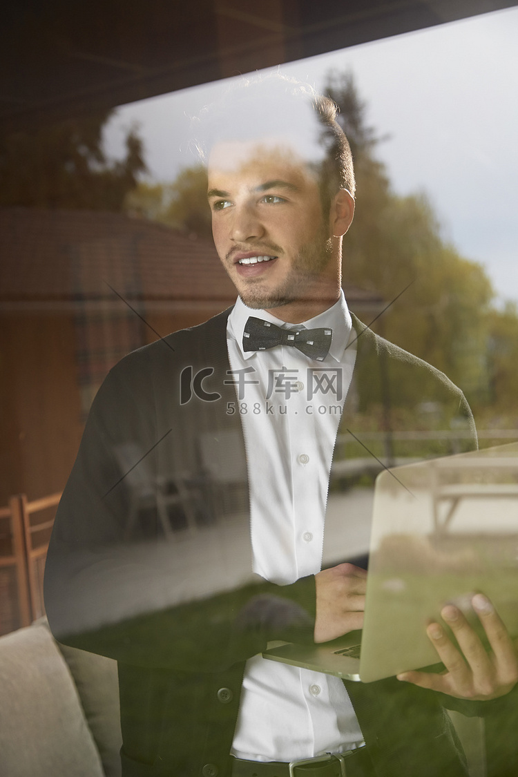 一名男子站在窗外看着手持笔记本