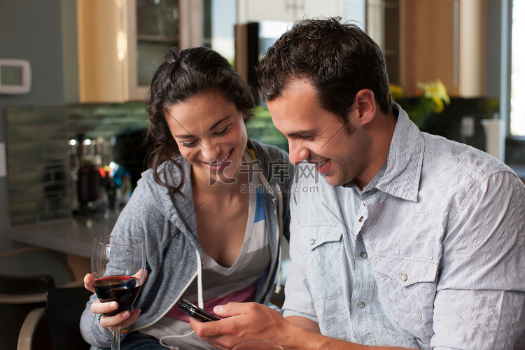一对年轻夫妇拿着酒杯看着手机